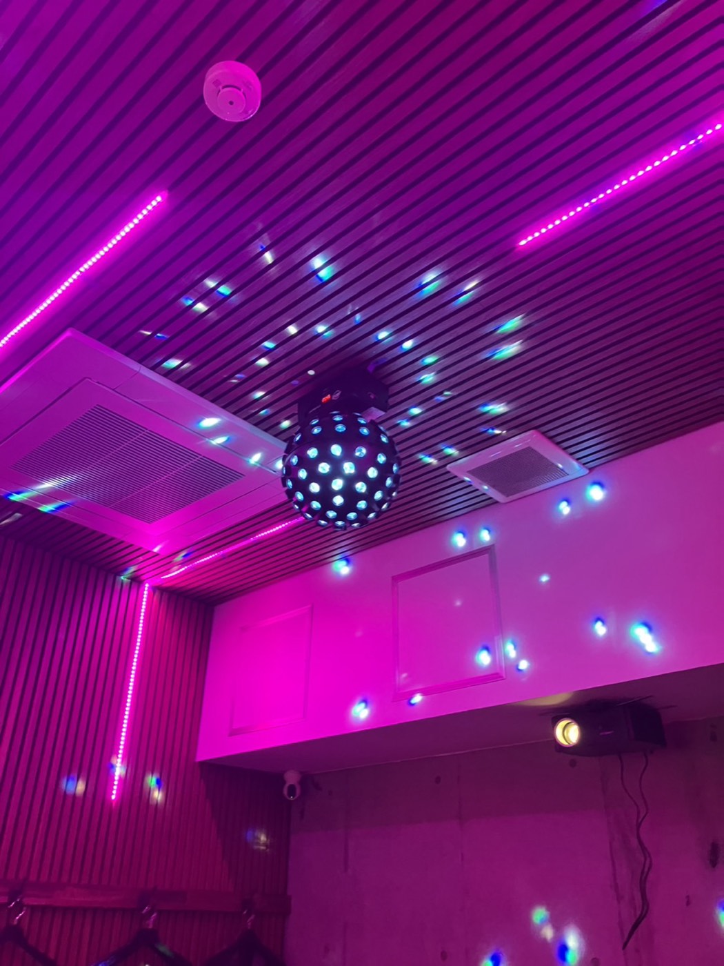 夜酒並木の個室カラオケ。回転するミラーボールが天井に光を散らし、ピンクのLEDラインと、壁際に設置されたプロジェクターが見える